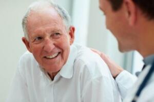 An elderly man speaking with his care provider, smiling thanks to restorative dentistry.